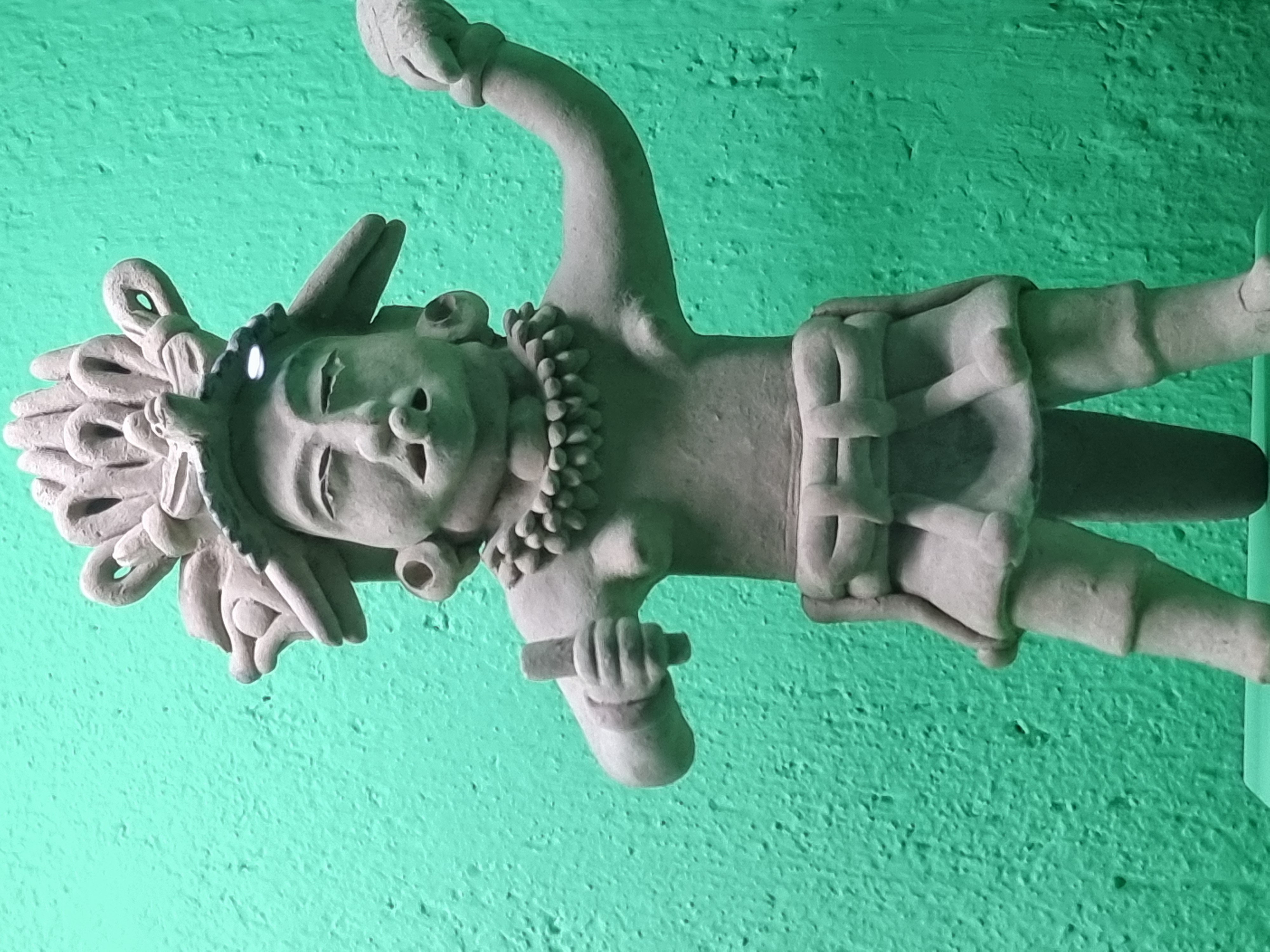 Figurine maya coiffée sur mur turquoise Mexique